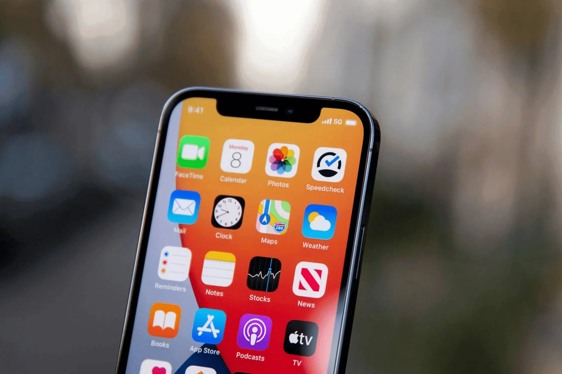 Bovenkant van een iPhone met het beginscherm en 5G in de statusbalk, buiten met onscherpe achtergrond