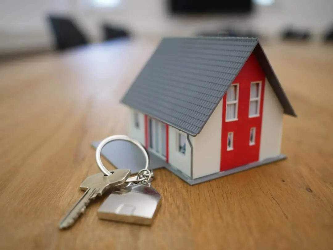 Modelhuisje op een houten tafel met daarvoor een sleutel aan een huisvormige sleutelhanger