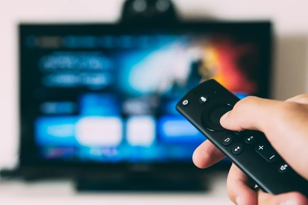 Hand met een afstandsbediening gericht op een televisie met een onscherp streamingmenu