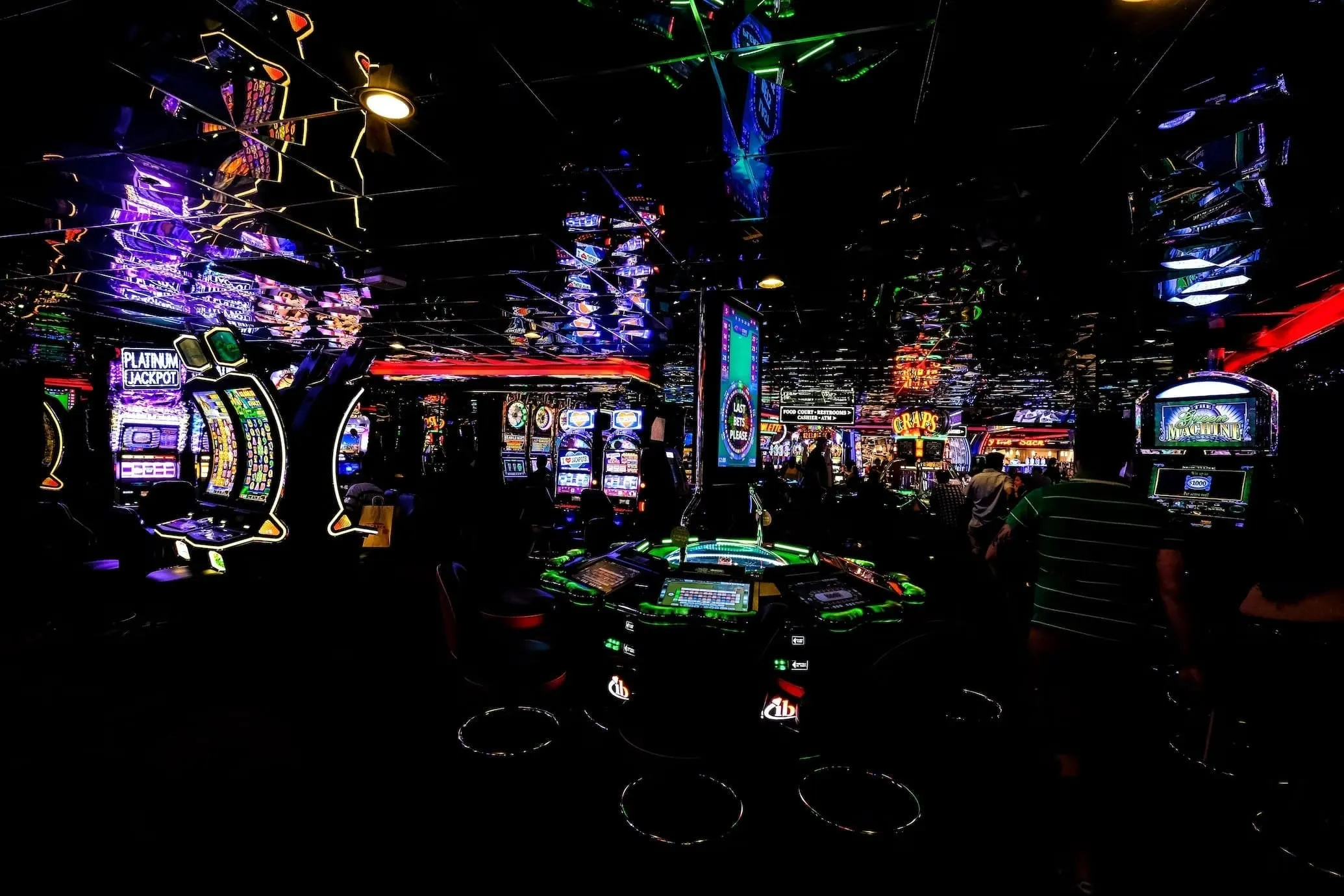 Donkere casinozaal met verlichte gokkasten en een roulettetafel onder een spiegelend plafond