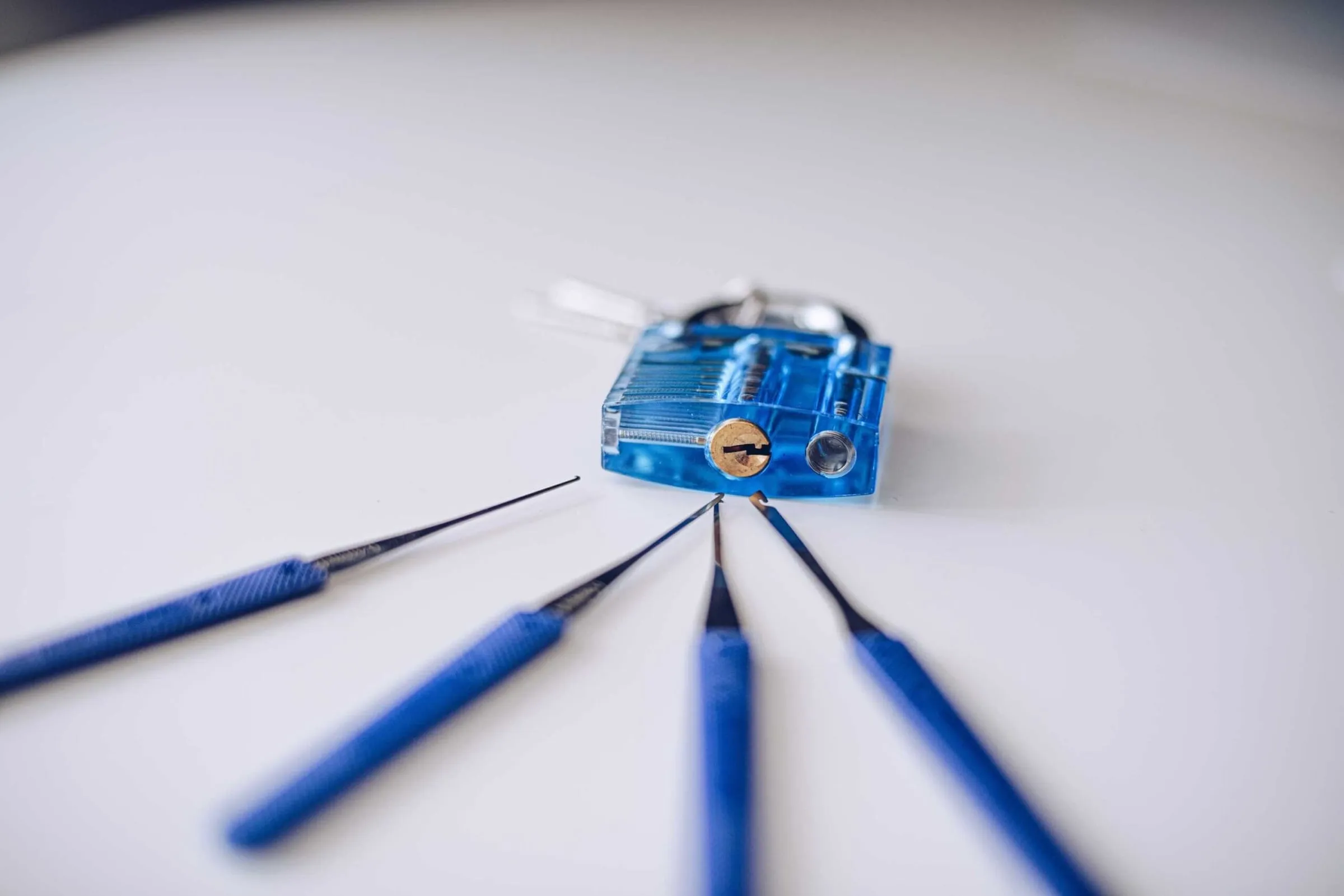 Doorzichtig blauw oefenslot met vier lockpicks met blauwe handgrepen ervoor uitgelegd