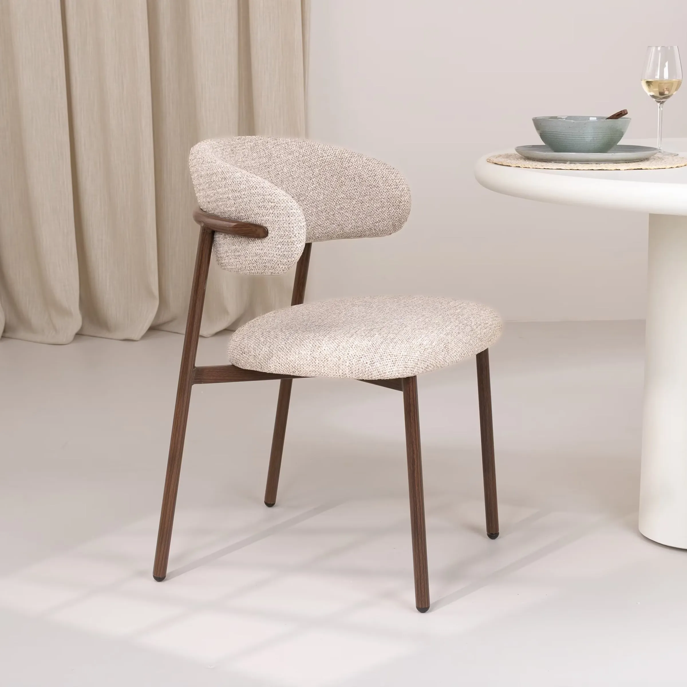 Japandi eetkamerstoel met bouclé zitting en donker houten frame naast een ronde witte tafel