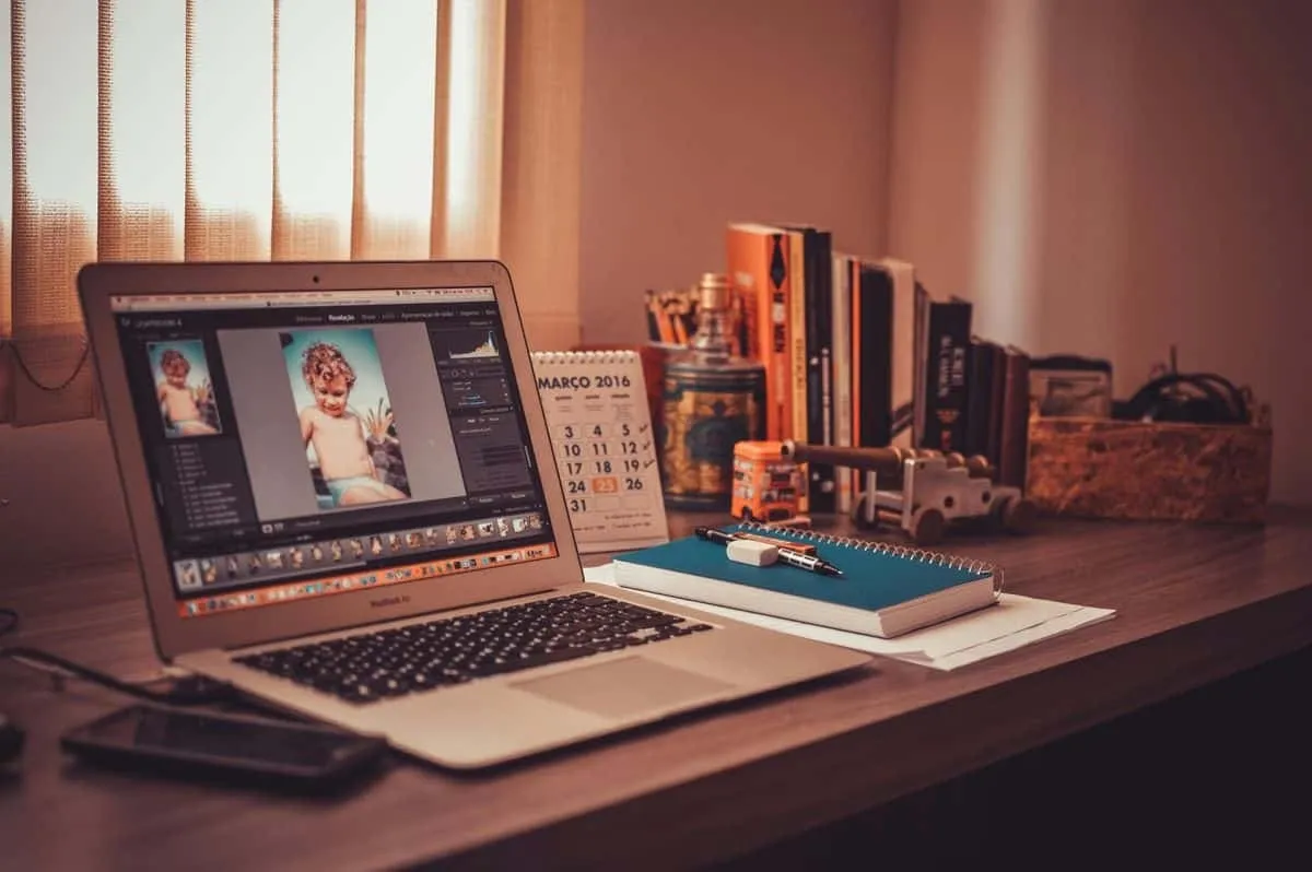 Bureau met een laptop waarop fotobewerkingssoftware openstaat, met een notitieblok, kalender en boeken ernaast