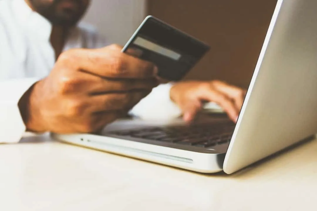 Man houdt een bankpas vast terwijl hij met zijn andere hand op een laptop typt