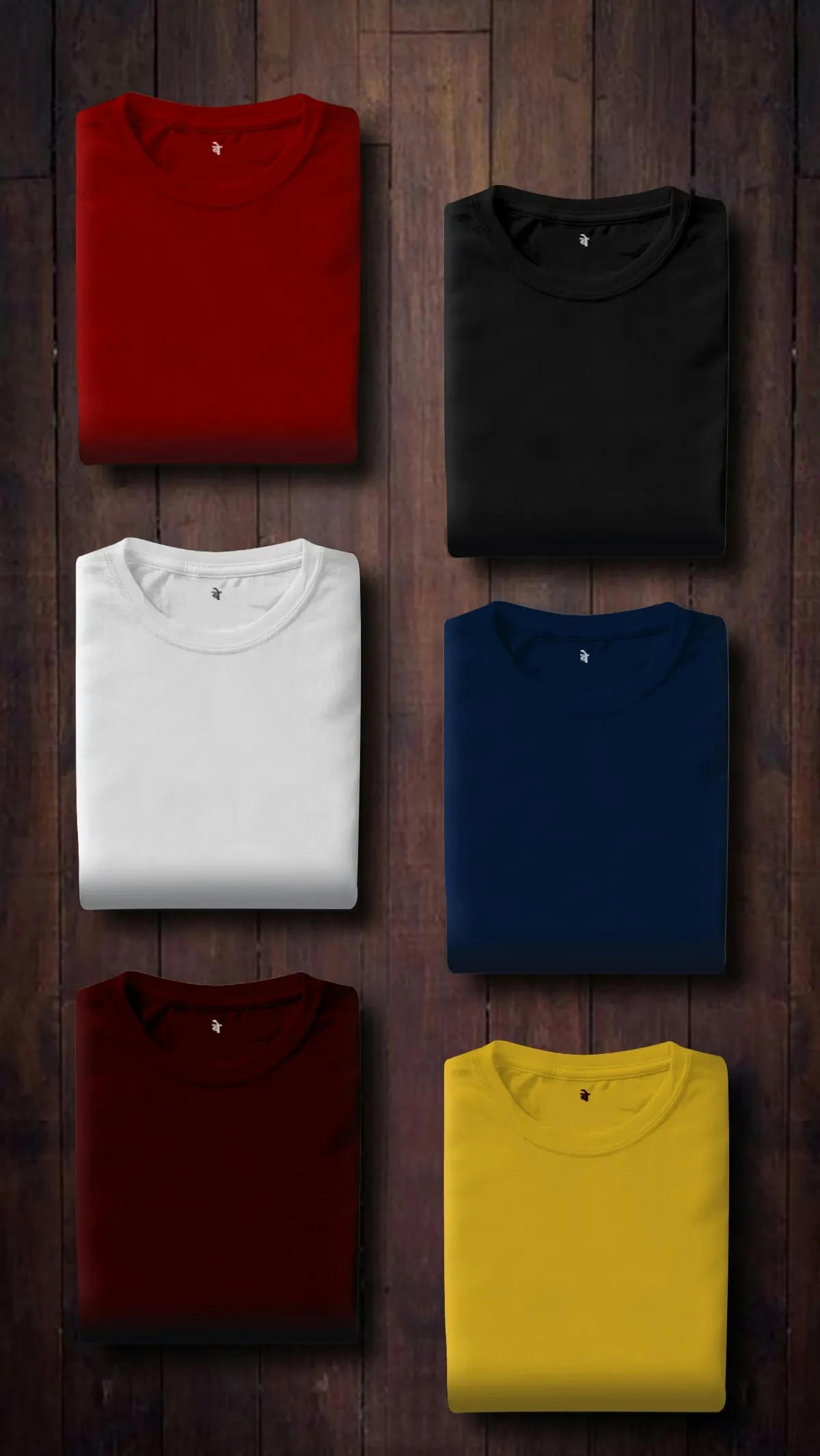 Zes opgevouwen T-shirts in rood, zwart, wit, marineblauw, bordeaux en geel naast elkaar op een donkere houten ondergrond
