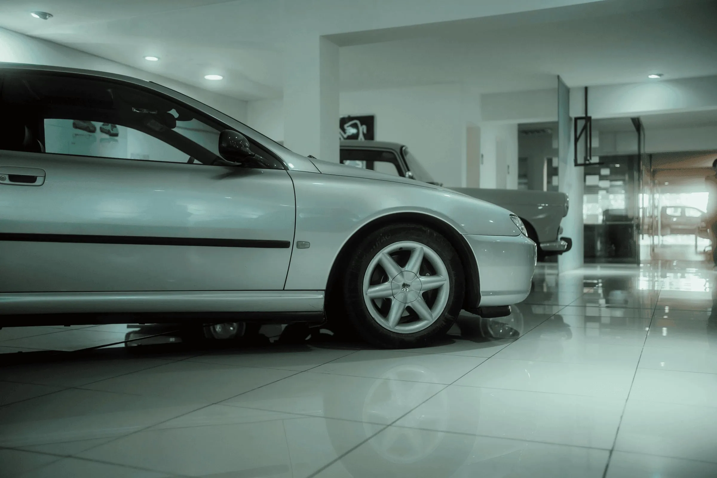 Zilverkleurige auto in een autoshowroom met een witte tegelvloer